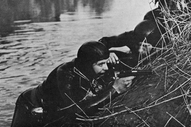 Ein Armeetaucher mit gezogener Pistole, an einem Damm liegend